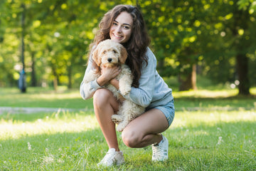 Woman holding a small dog in a park with green grass and trees